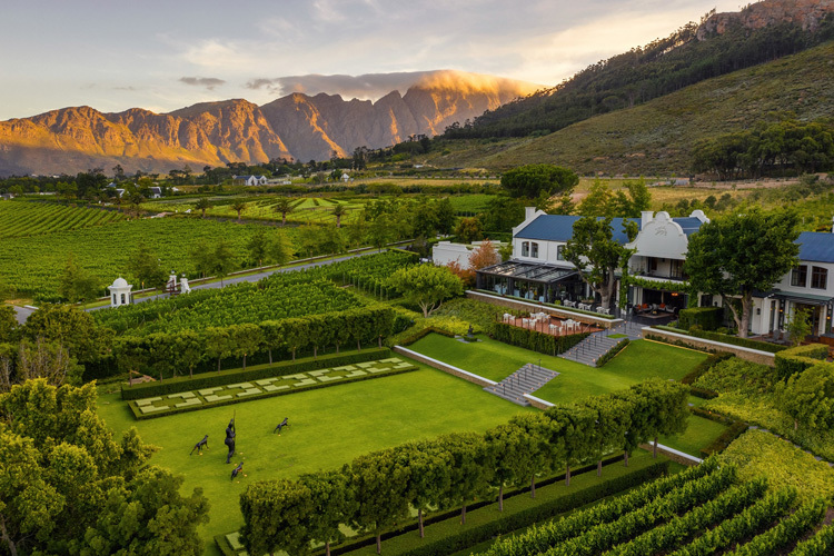 Franschhoek wine estate with manicured gardens and vineyards beneath mountains at golden hour
