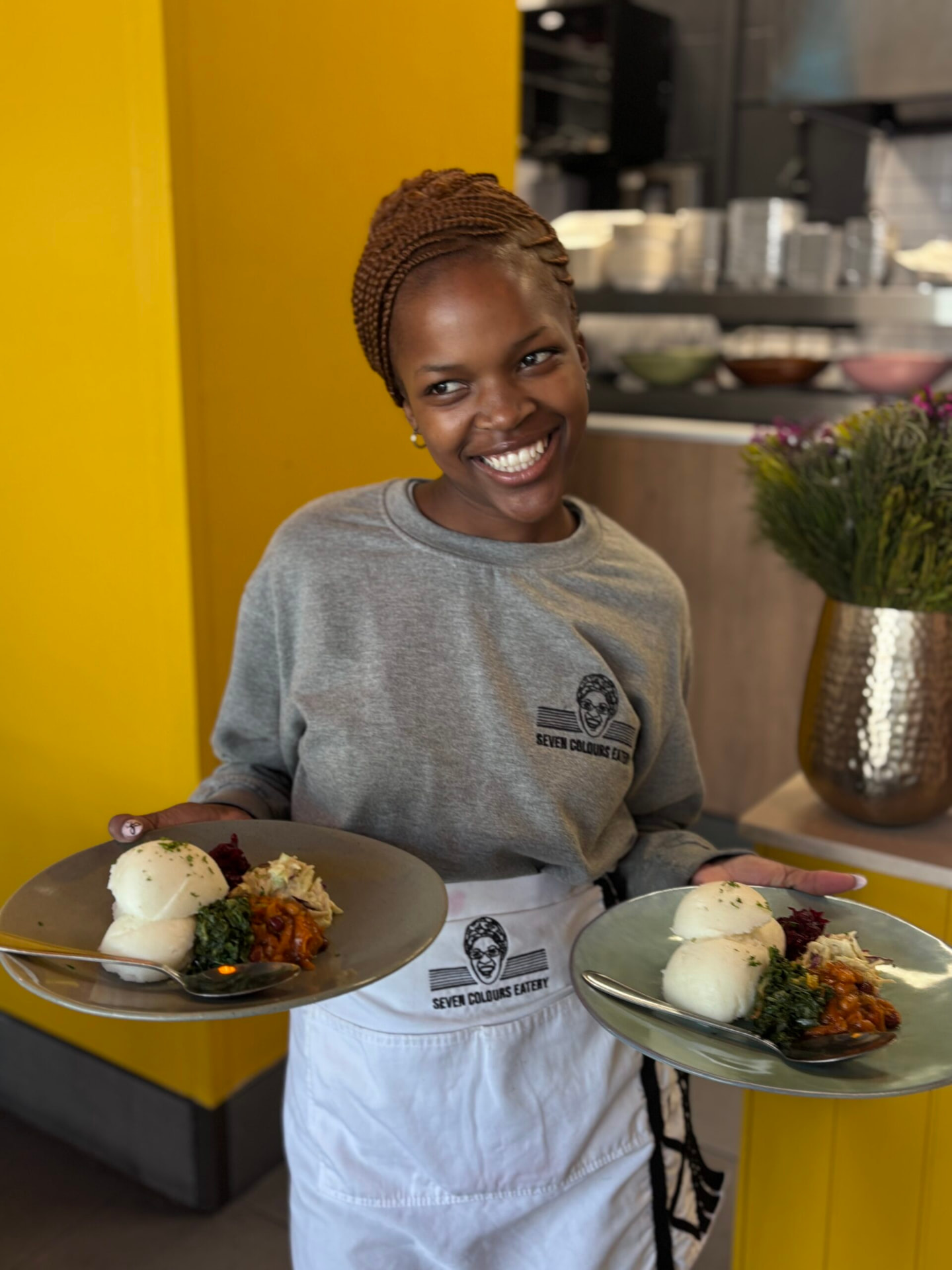 Smiling waitress carrying two plates of traditional South African food at a Cape Town eatery