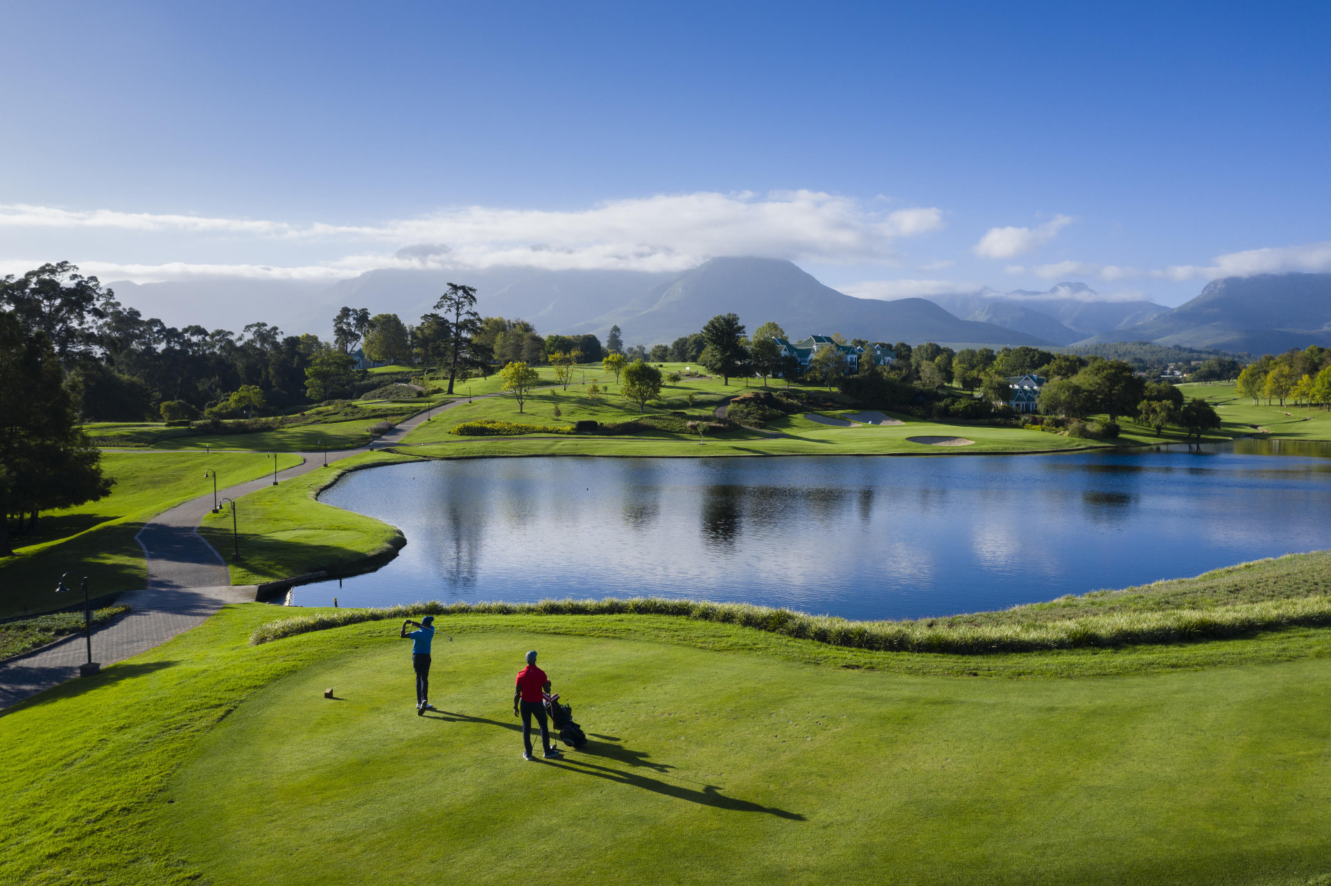 Golfers teeing off beside a lake with the Outeniqua mountains behind