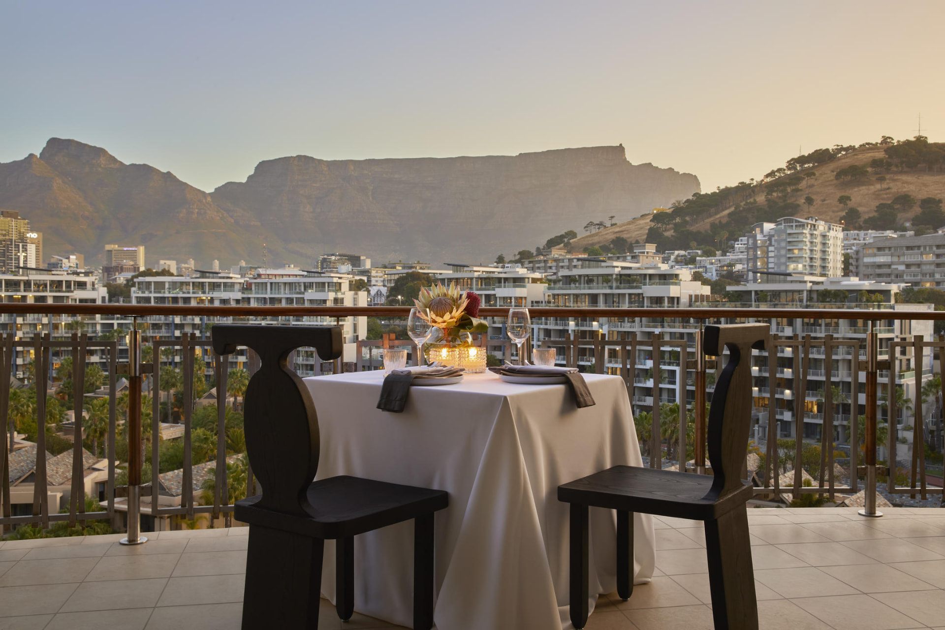 Table set for two on a hotel terrace at dusk with Table Mountain beyond the city