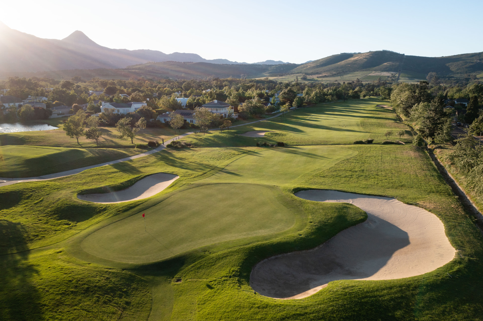 Aerial view of a green and bunkers at Erinvale with the Helderberg mountains beyond in golden light